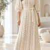 Ivory crochet midi dress with vertical cable braids, three-quarter puff sleeves, ribbed cuffs, and a matching waist sash
